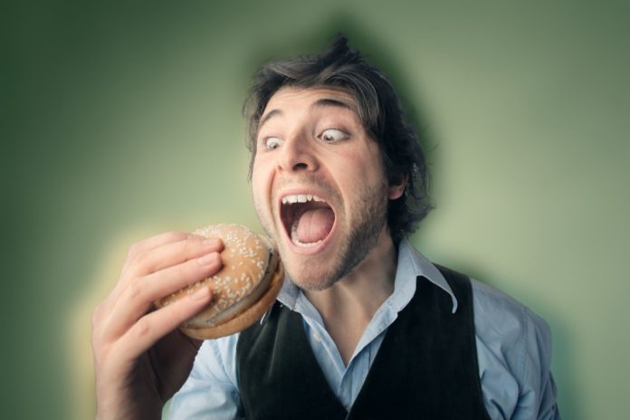 Homem com hambúrguer na mão para ilustrar a fome de besteira